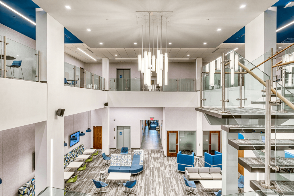 view of two-story office with modern light fixtures, blue and green chairs, and bright white walls