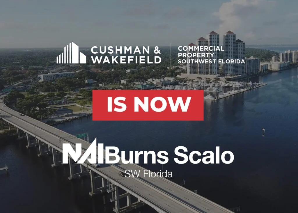 The image features a scenic aerial view of a waterfront area with a bridge crossing over water, surrounded by greenery and buildings. Prominently displayed are the logos for "Cushman & Wakefield" and "NAI Burns Scalo," along with the text "IS NOW" in bold red. The background includes high-rise buildings and a clear sky.